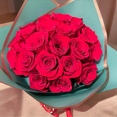 Bouquet of bright pink roses wrapped in teal paper with ribbon