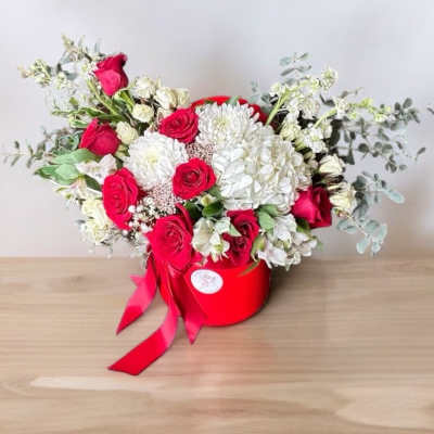 Red and white rose arrangement in a red hat box with ribbon