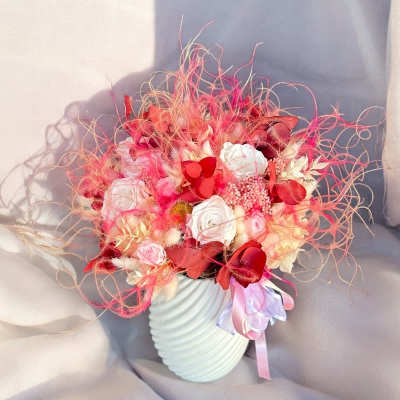 Pink and red floral arrangement in a white vase with ribbon