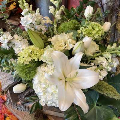 White lilies and hydrangeas arranged with green accents in a rustic container
