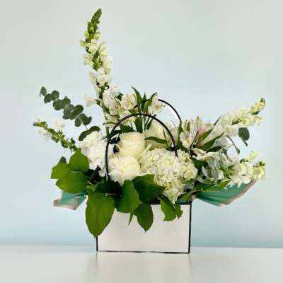 White floral arrangement in a white box with black handles