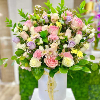 Pastel pink, white, and lavender flower arrangement in a white hatbox with ribbon
