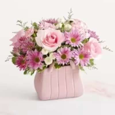 Pink roses and daisy poms arranged in a pink purse-shaped ceramic container
