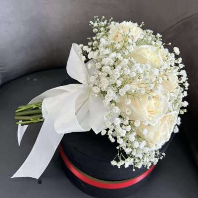 Cream rose bouquet with baby's breath and a white ribbon on a black hat box