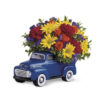 Mixed bouquet of yellow daisies, red carnations, and orange roses in a blue ceramic toy truck.