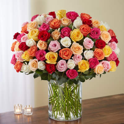 Large mixed-color rose arrangement in a clear glass vase on a wooden table