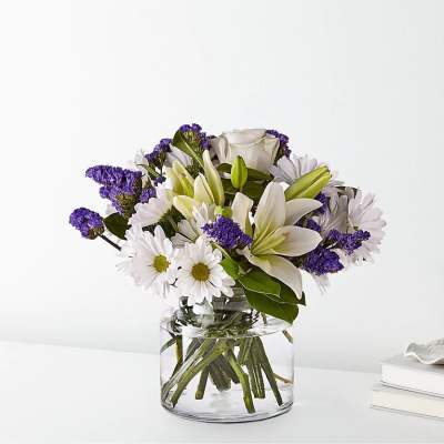 White daisies, lilies, roses, and purple blooms arranged in a clear glass vase.