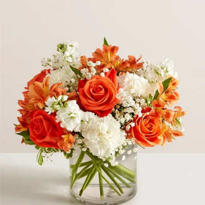 Compact bouquet of orange roses and white flowers in a clear glass vase
