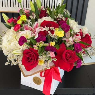 Mixed bouquet of red roses, lilies, and pink flowers in a white box with a red ribbon