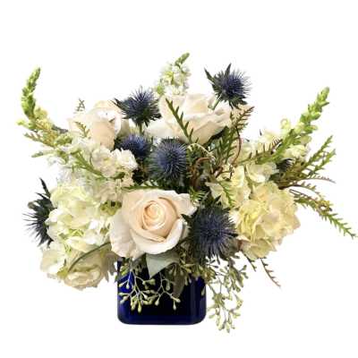 White roses and pale blooms in a blue vase with spiky blue thistles