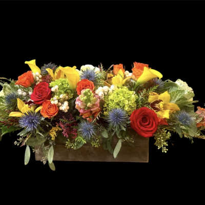 Long floral arrangement in a wooden box with red, yellow, and orange blooms