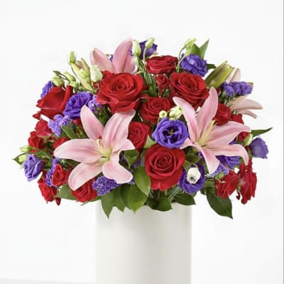 Bouquet of red roses, pink lilies, and purple blooms in a white vase