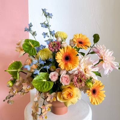 Mixed bouquet in a pink vase with orange, pink, blue, and white flowers
