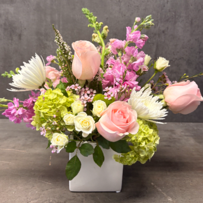 Pastel arrangement of pink roses, white mums, and green hydrangeas in a white cube vase