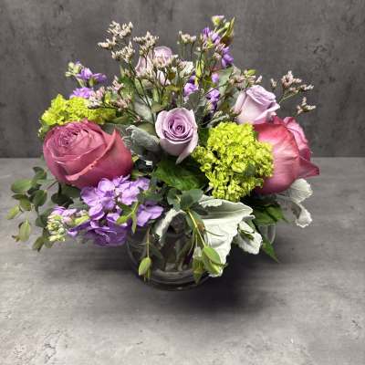 Pink and lavender roses arranged in a glass vase with purple blooms