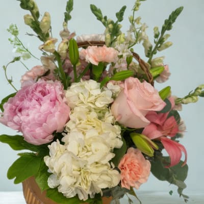 Pink and white floral arrangement in a round basket container