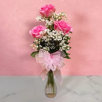 Pink roses in a clear glass vase with baby's breath and a pink bow