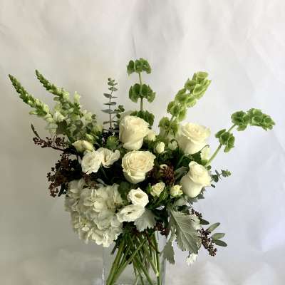 White floral arrangement in a clear square vase with tall green accents