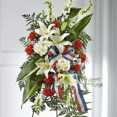 Standing floral spray with white lilies, red carnations, and a ribbon on an easel