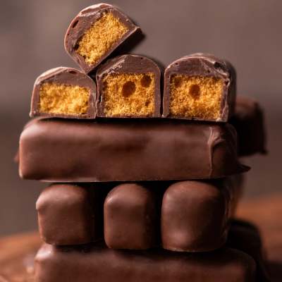 Stack of chocolate-covered candy bars with golden crunchy centers, some cut to show the inside.