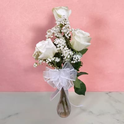 White roses and baby's breath in a clear glass vase with a white bow