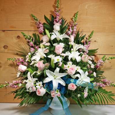 White lilies and pink roses arranged in a white vase with a blue ribbon