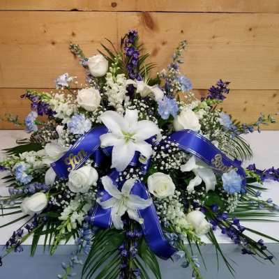 White lilies and roses with blue flowers and ribbon in a low arrangement