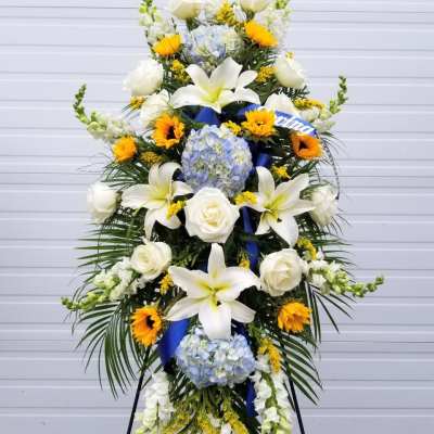Tall standing floral spray with white lilies, roses, hydrangeas, and sunflowers