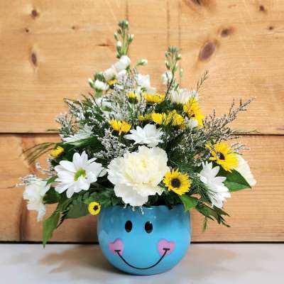 White and yellow flowers arranged in a blue smiley-face pot