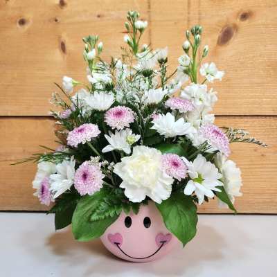 Pink smiley-face pot holding white and pale pink flowers