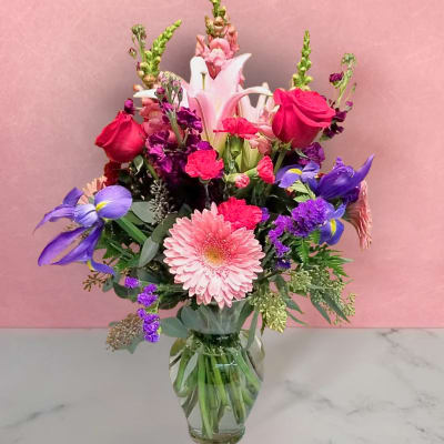 Mixed bouquet with pink lilies, roses, and purple flowers in a glass vase