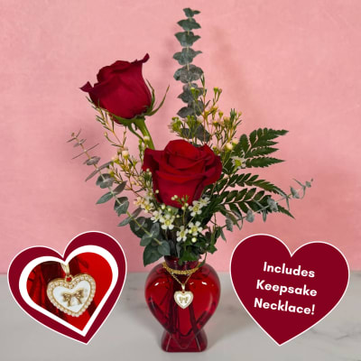 Two red roses in a red heart-shaped vase with a necklace pendant