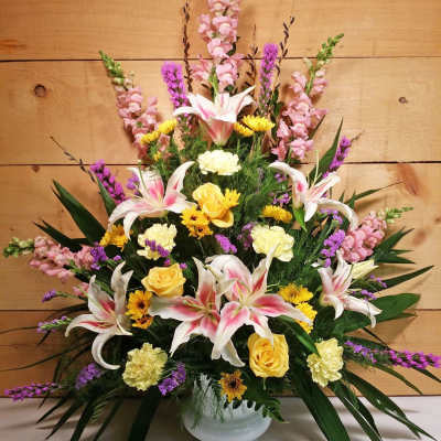 Pink lilies and yellow roses in a white vase with purple accents