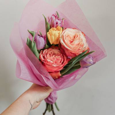 Handheld bouquet of pink and peach tulips wrapped in pink paper