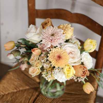 Mixed pastel bouquet in a glass vase on a wooden chair