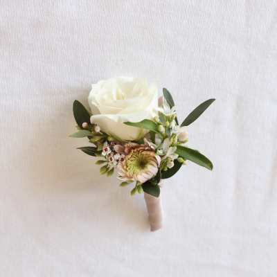 White rose boutonniere with small pink flowers and greenery