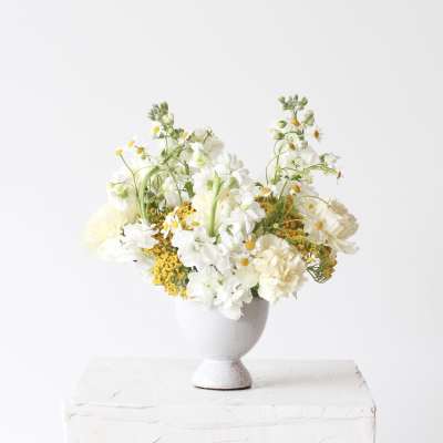 White and pale yellow flowers arranged in a gray pedestal vase
