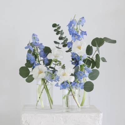 Blue and white flowers in clear glass vases with round greenery