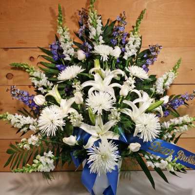 White lilies and chrysanthemums with blue ribbon on a sympathy spray