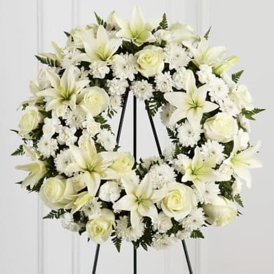 White floral wreath on a black stand with lilies and roses