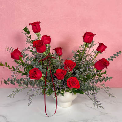 Arrangement of red roses in a white vase with trailing greenery