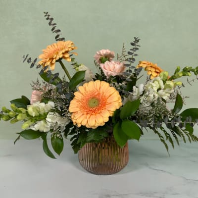 Peach gerbera daisies and pale pink carnations in a ribbed glass vase