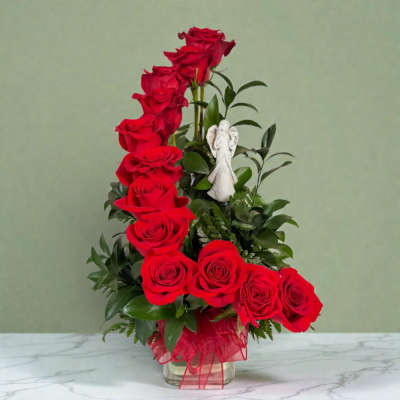 Red roses arranged in a clear glass vase with a small angel figurine