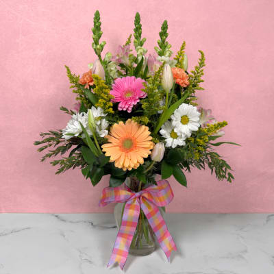 Mixed bouquet of pink, peach, and white flowers in a glass vase with plaid ribbon