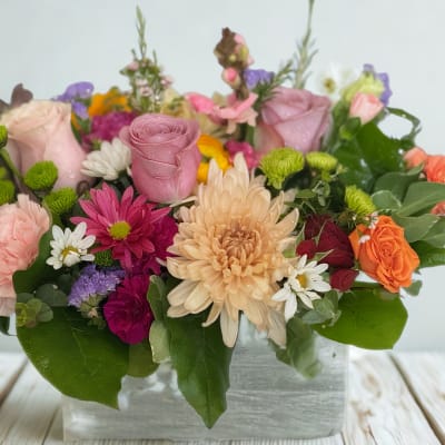 Mixed bouquet of pink, peach, orange, and white flowers in a clear vase