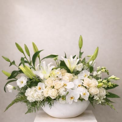 White lilies, roses, and orchids arranged in a white bowl vase