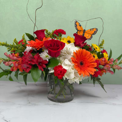 Mixed bouquet of red, orange, white, and yellow flowers in a glass vase