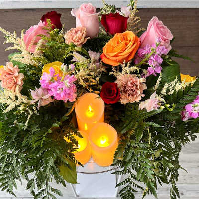 Mixed bouquet with roses, carnations, and candles in a white container