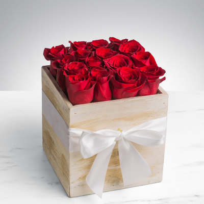 Red roses arranged in a square wooden box with a white ribbon
