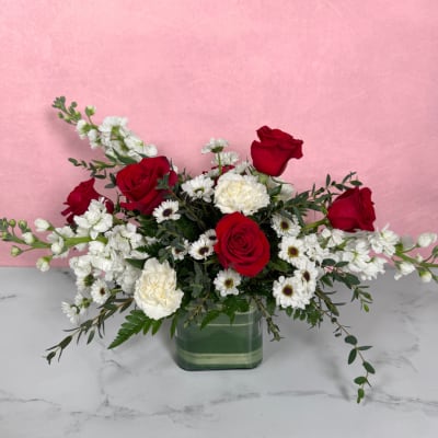 Red roses and white flowers arranged in a square glass vase